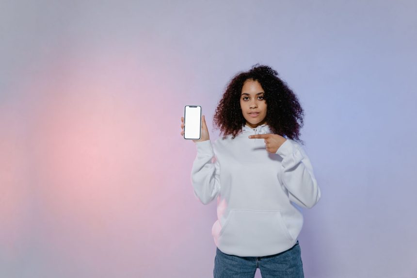 Mulher aponta para a tela em branco de um smartphone, em uma composição que remete ao uso de aplicativos de saúde e à publicidade digital.
