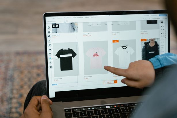 Pessoa aponta para opções de camisetas exibidas em uma loja virtual na tela de um laptop