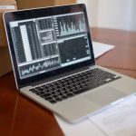 Laptop exibindo gráficos e métricas sobre uma mesa, ao lado de caixas de papelão, em um ambiente de pequeno negócio.