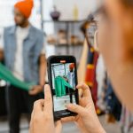 Pessoa fotografa uma jaqueta verde com o celular em uma loja de roupas.