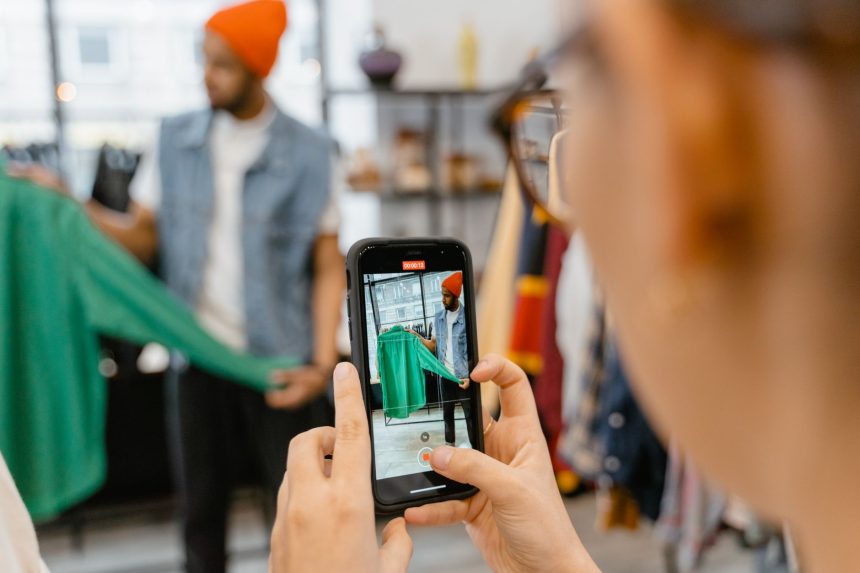 Pessoa fotografa uma jaqueta verde com o celular em uma loja de roupas.