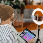 Criador de conteúdo grava um podcast usando tablet e celular em um estúdio doméstico com iluminação circular.