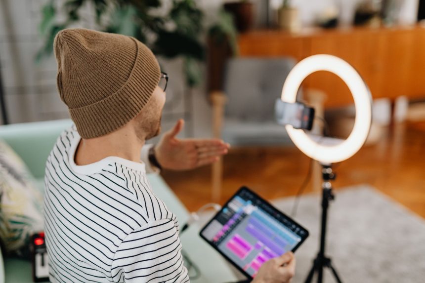 Criador de conteúdo grava um podcast usando tablet e celular em um estúdio doméstico com iluminação circular.