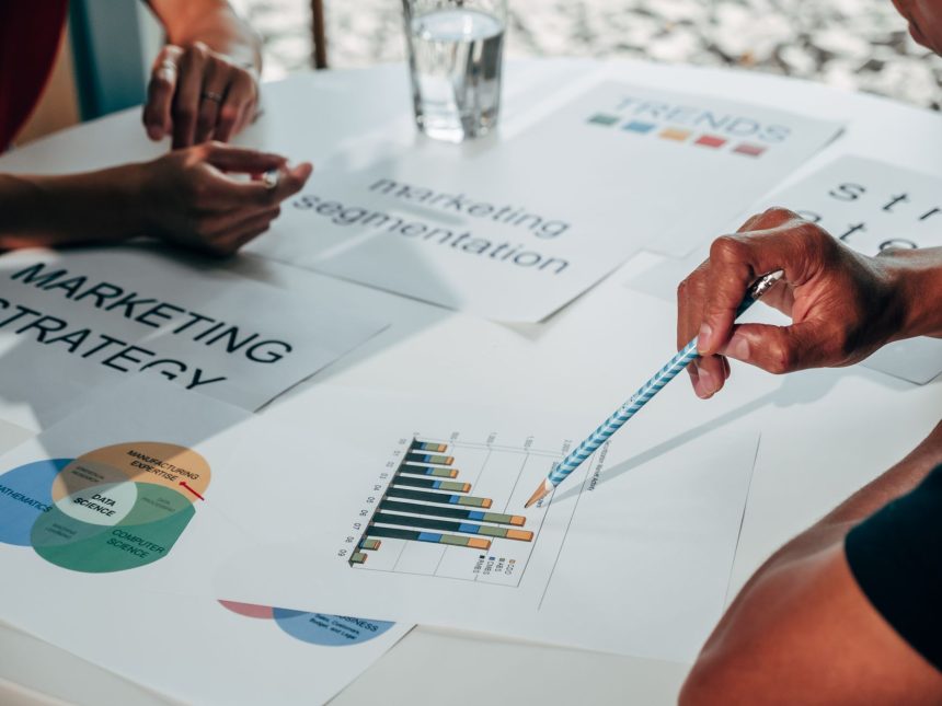 Equipe reunida em um escritório analisa gráficos, documentos e dados para desenvolver uma estratégia de marketing.