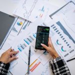 Vista superior de gráficos e um smartphone sobre uma mesa de escritório, representando análise de dados digitais.