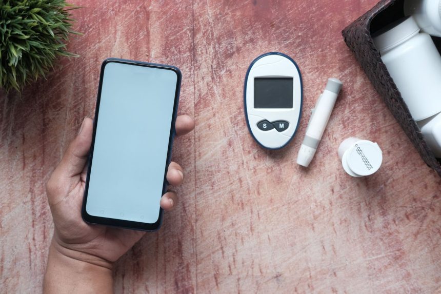 Mão segurando um smartphone ao lado de um glicosímetro e materiais médicos sobre uma superfície de madeira.