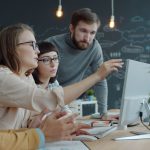 Equipe diversa reúne-se diante de um computador em um espaço de trabalho moderno para discutir ideias.