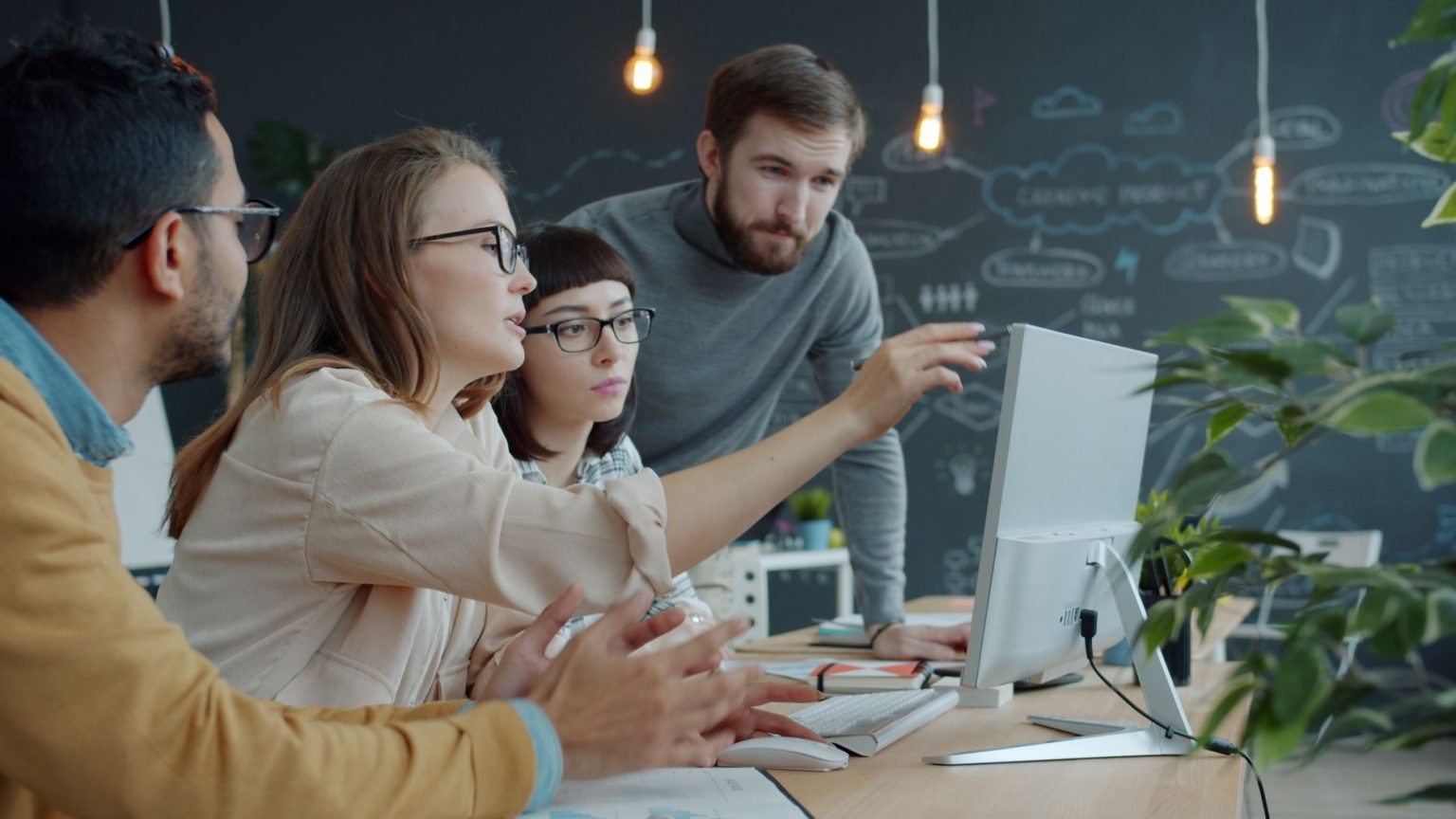 Equipe diversa reúne-se diante de um computador em um espaço de trabalho moderno para discutir ideias.