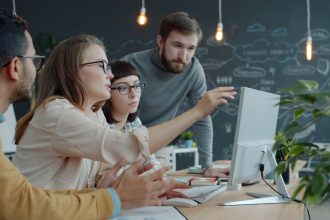 Equipe diversa reúne-se diante de um computador em um espaço de trabalho moderno para discutir ideias.