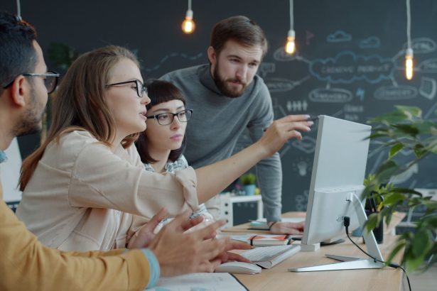Equipe diversa reúne-se diante de um computador em um espaço de trabalho moderno para discutir ideias.